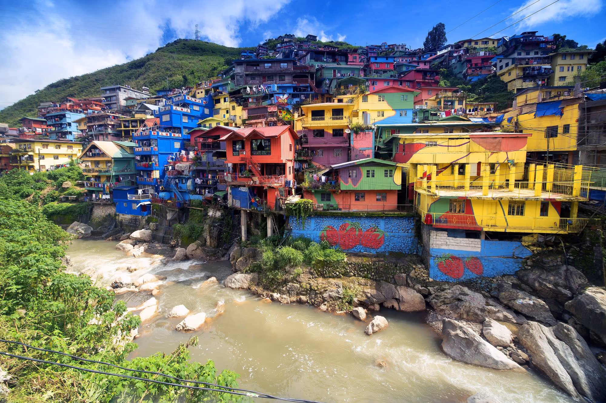 The brightly painted houses of StoBoSa in La Trinidad, next to Baguio, stacked up a green hillside above the Balili River.