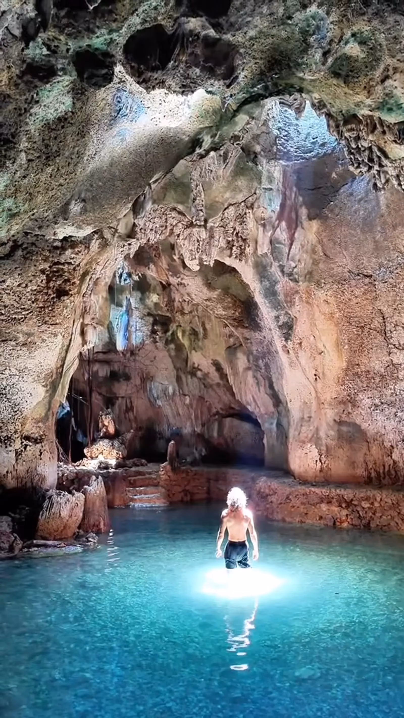 Robert standing waist-deep in a glowing blue pool at the bottom of a limestone cave, light falling in from above.
