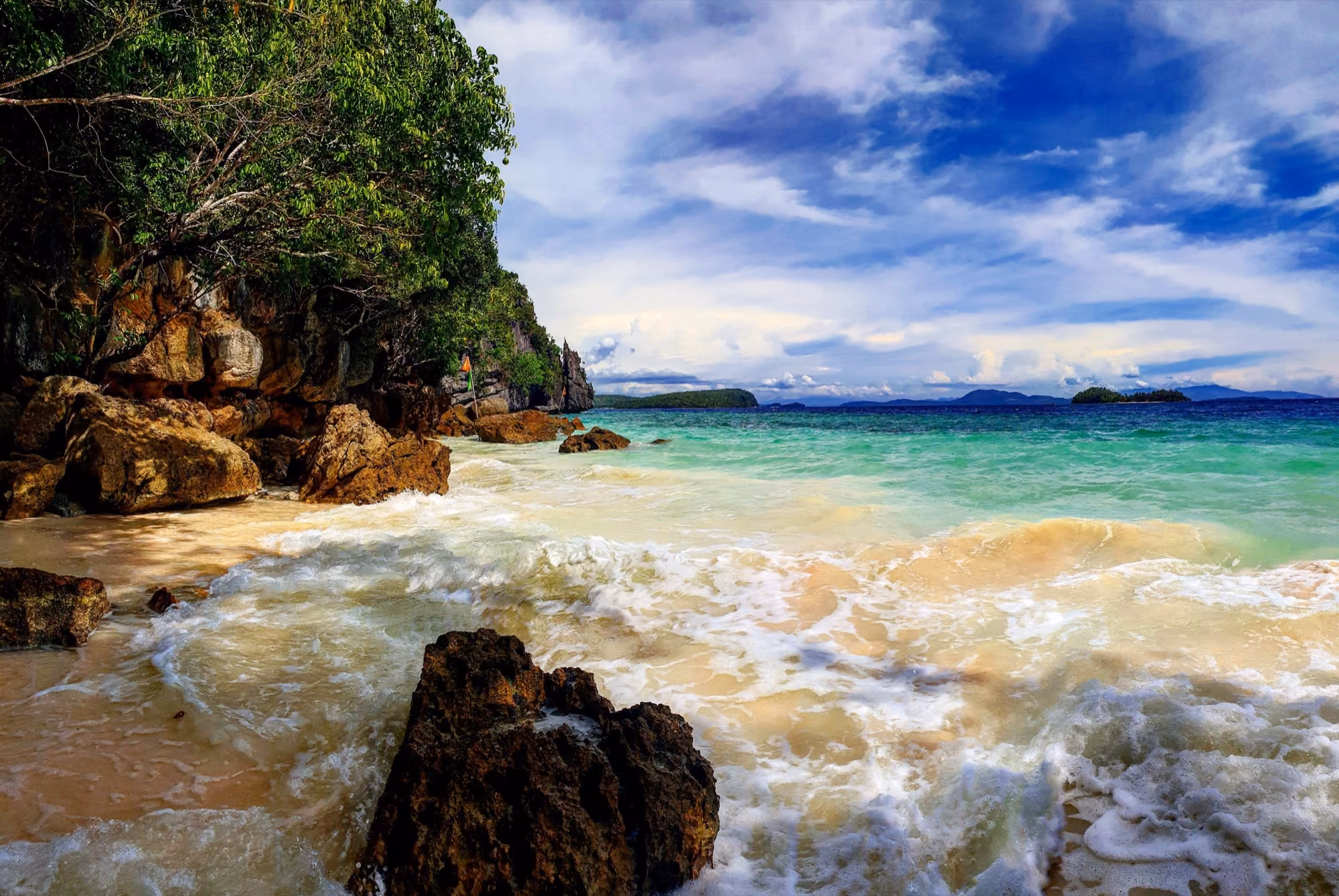 A beach on Dinagat Island with rocks in the foreground, turquoise water and a blue sky with clouds.
