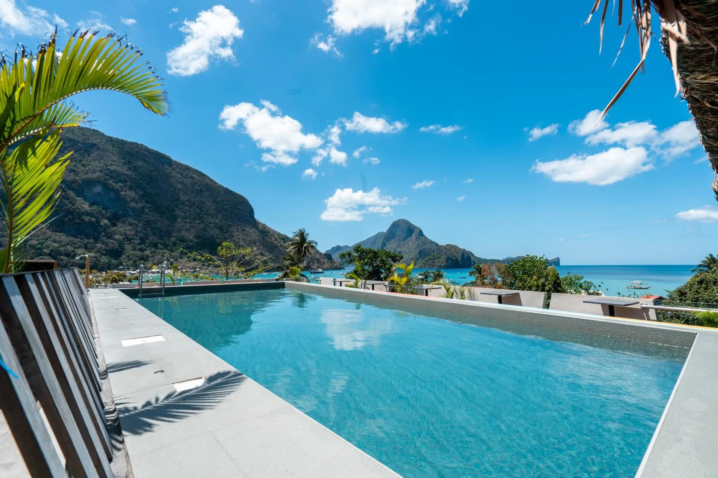 The rooftop pool at Frendz Hostel El Nido, with sun loungers and a view over El Nido bay and its limestone cliffs under a blue sky.