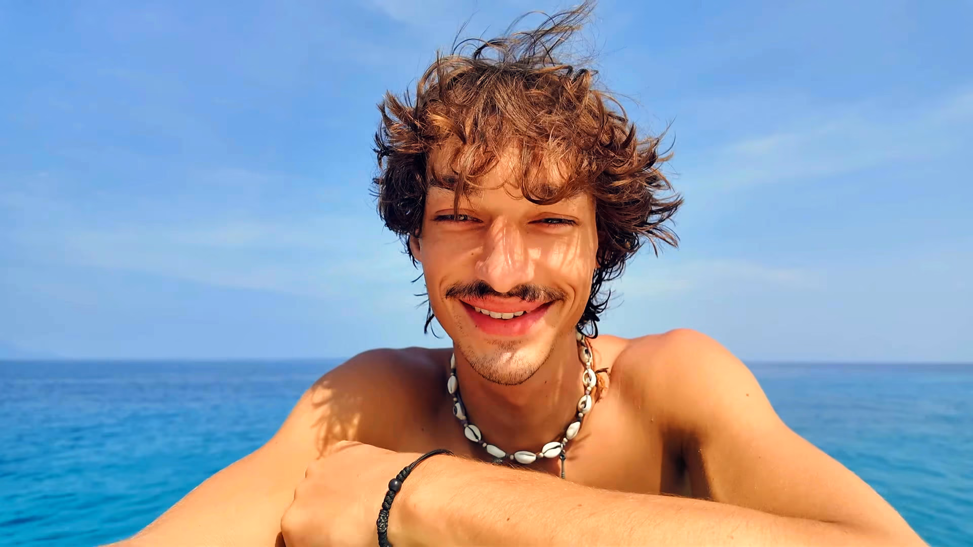 Robert smiling into the camera with the open sea and a clear sky behind him.