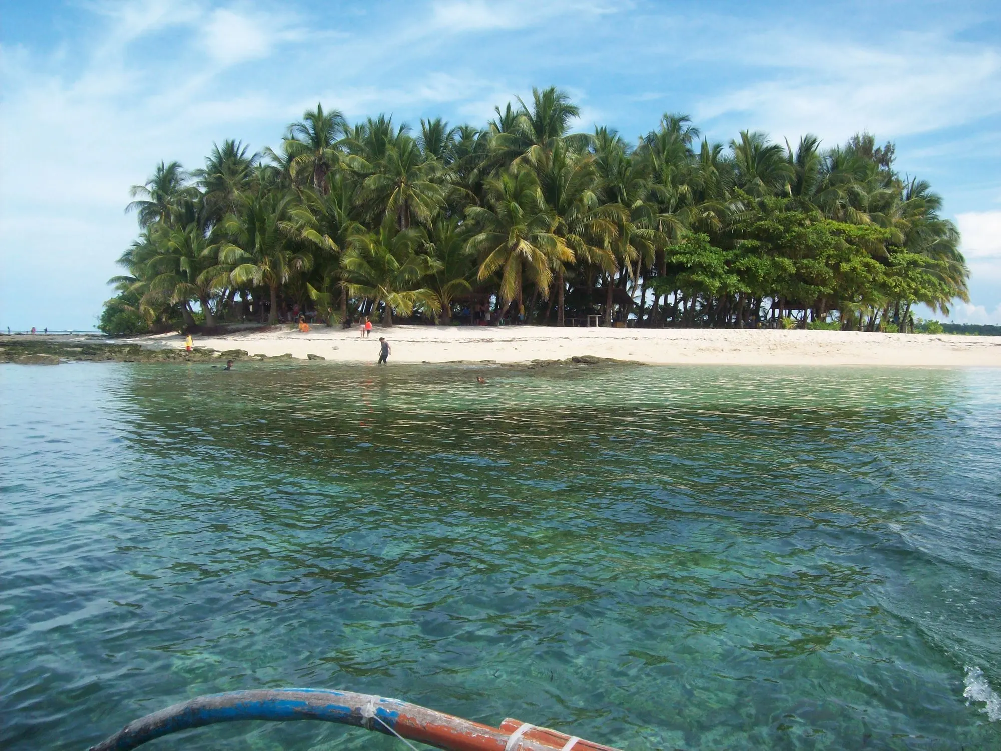 Guyam Island off Siargao: a small island of coconut palms and white sand, seen across clear turquoise water from a boat.