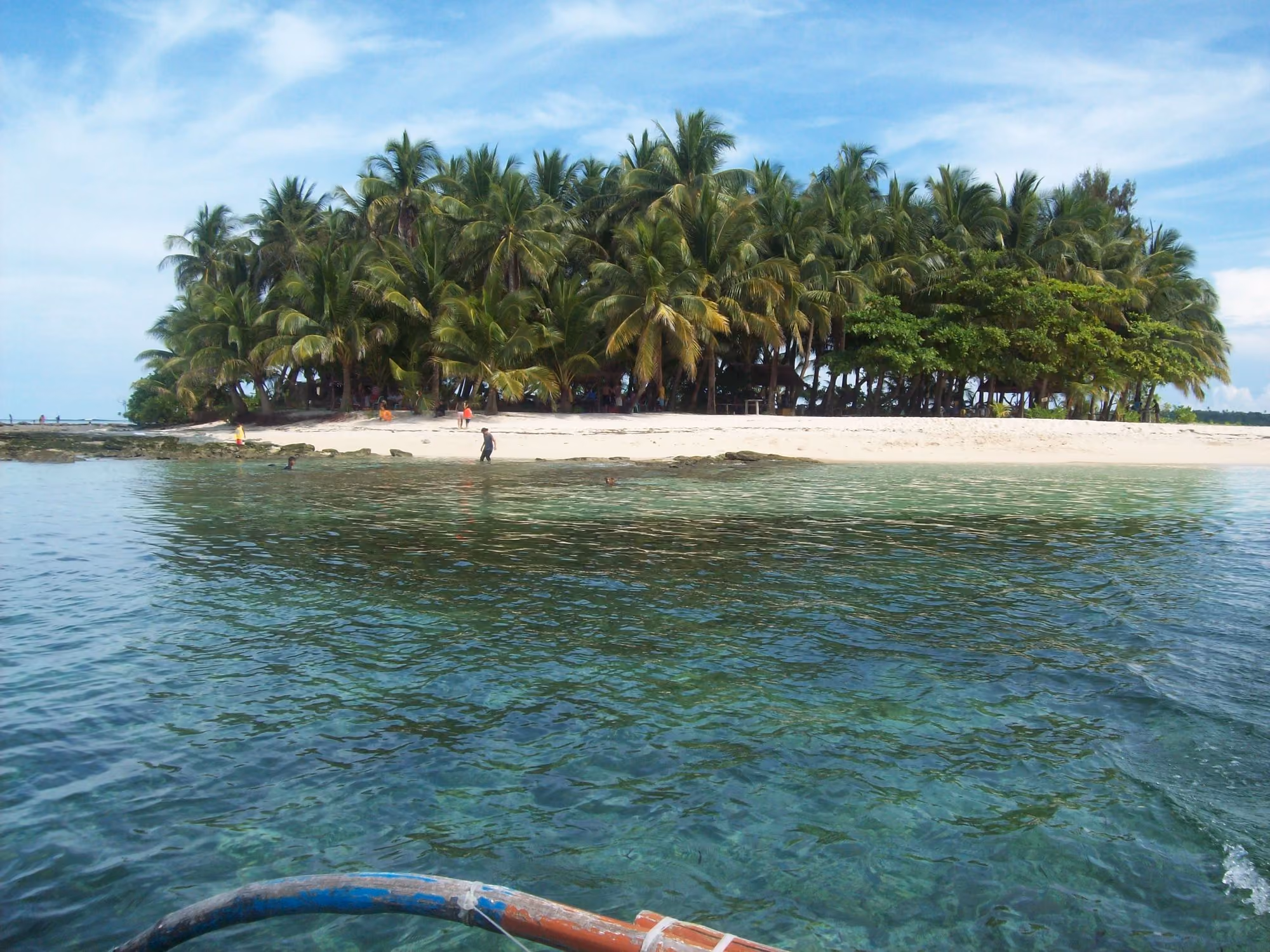Guyam Island off Siargao: a small island of coconut palms and white sand, seen across clear turquoise water from a boat.