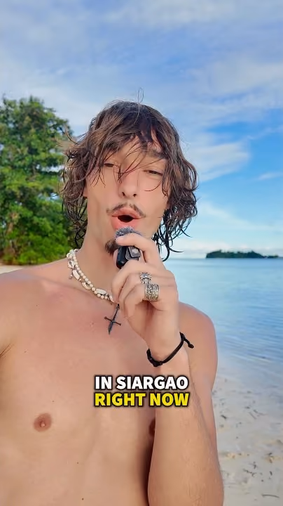 Robert on a beach in Siargao, talking into the camera, with a small island on the horizon behind him.
